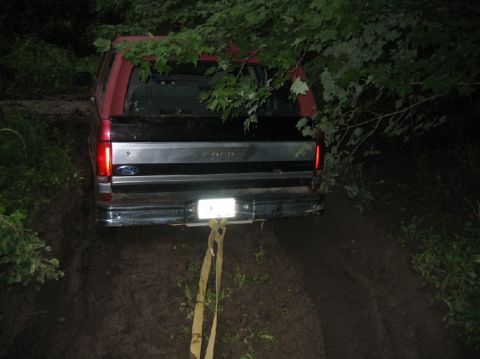1995 Ford Bronco - A red and black Ford F-Series truck is stuck in the mud, viewed from the rear with a tow strap attached.