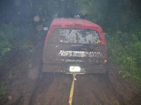 1995 Ford Bronco - A red SUV is stuck in thick mud on a trail, with a tow strap attached to its rear.