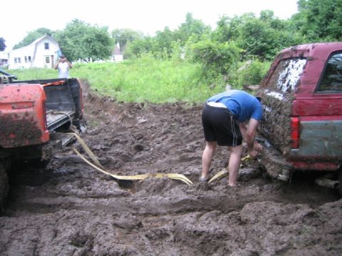1995 Ford Bronco - Two vehicles are deeply stuck in mud, with a person working to free the red SUV.