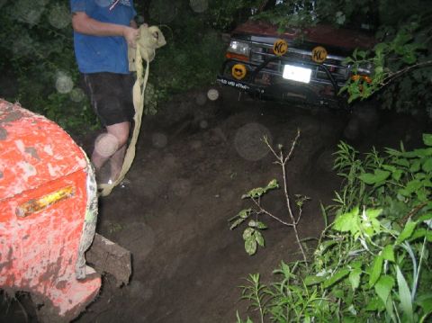 1995 Ford Bronco - A red 1995 Ford Bronco is stuck in the mud, with a winch strap being handled by a person nearby.