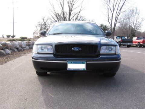 1999 Ford Crown Victoria - The front grille and headlights of a 1998 Ford Crown Victoria are visible, with other vehicles in the background.