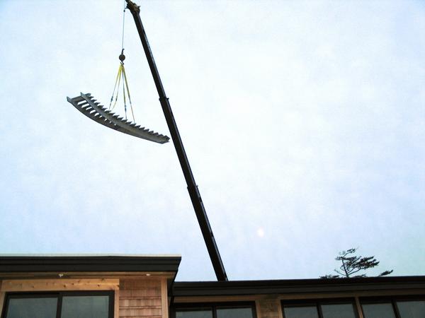 Crane lifting a metal rake-like object over a building