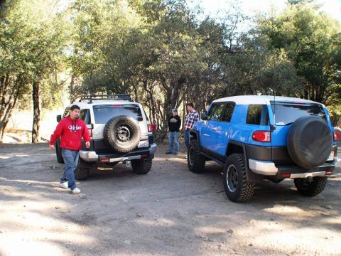 2007 Toyota FJ Cruiser - Two Toyota FJ Cruisers are parked on a dirt road surrounded by trees, with several people present.
