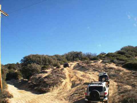 2007 Toyota FJ Cruiser - Multiple Toyota FJ Cruisers navigate a steep, sandy off-road trail under a clear blue sky.