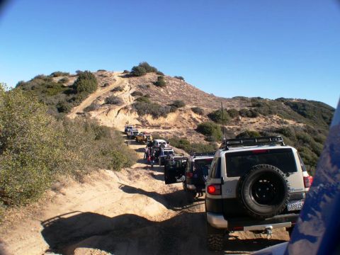 2007 Toyota FJ Cruiser - Multiple 2007 Toyota FJ Cruisers navigate a steep dirt trail on a sunny day.