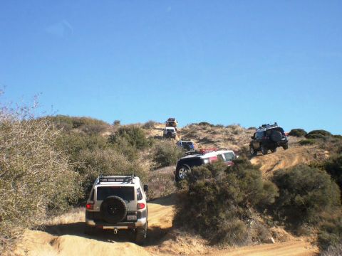 2007 Toyota FJ Cruiser - A convoy of Toyota FJ Cruisers navigates a challenging dirt path under a clear blue sky.