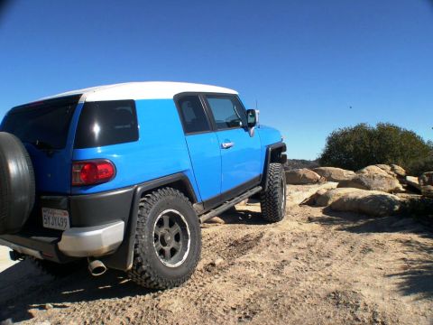 2007 Toyota FJ Cruiser - A blue and white 2007 Toyota FJ Cruiser is seen from the rear, parked on a rocky, dirt trail under a clear blue sky.