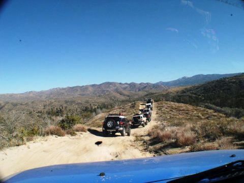 2007 Toyota FJ Cruiser - Multiple Toyota FJ Cruisers navigate a dusty trail through a dry, mountainous terrain under a clear blue sky.