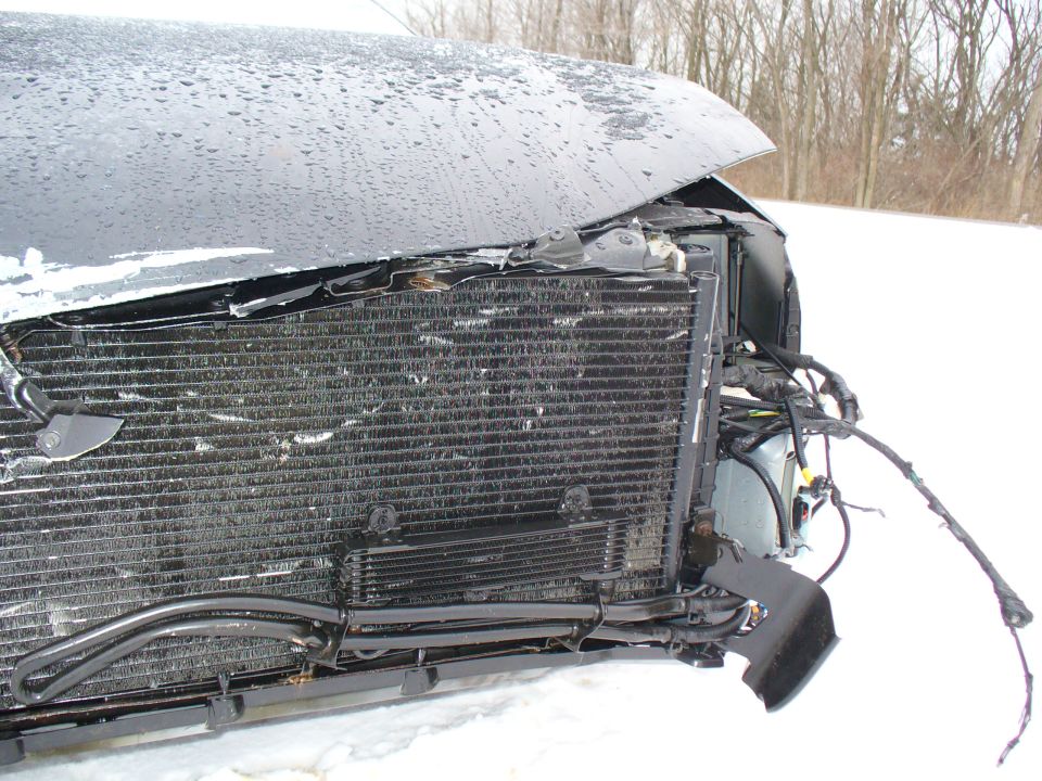 Front-end collision damage on a black car exposing radiator and wiring in snow