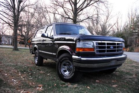 1993 Ford Bronco - This 1993 Ford Bronco is shown in a three-quarter front view, parked on a grassy area with trees in the background.