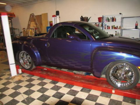 2004 Chevrolet SSR - A purple pickup truck with flame decals is shown on a red lift in a garage.