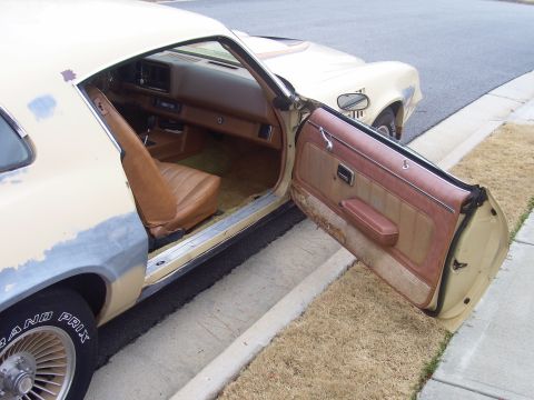 1979 Chevrolet Camaro - The interior of a 1979 Chevrolet Camaro is visible with the driver's door ajar, revealing tan upholstery and door trim.