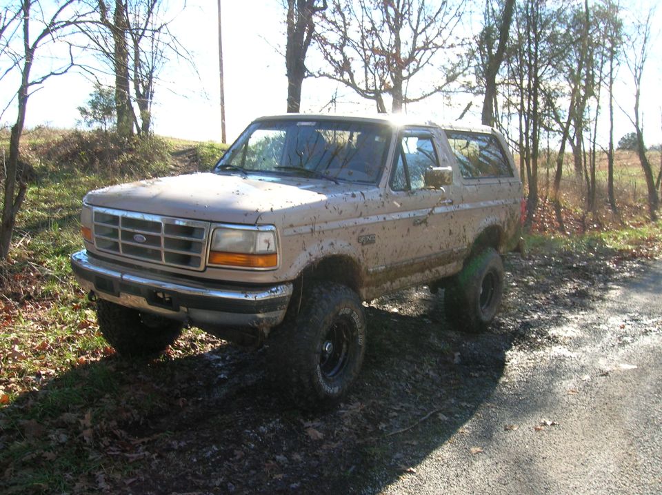 Mud-splattered 1996 Ford Bronco parked on a dirt road with trees in the background