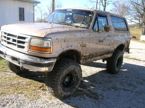 1996 Ford Bronco - A mud-covered Ford Bronco sits on a gravel lot, its body and tires caked with dirt.
