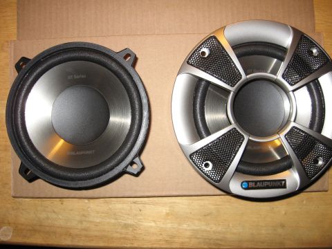 1992 Ford Crown Victoria - Two Blaupunkt car speakers, one with a silver mesh grille, are displayed on a wooden table with a cardboard backing.