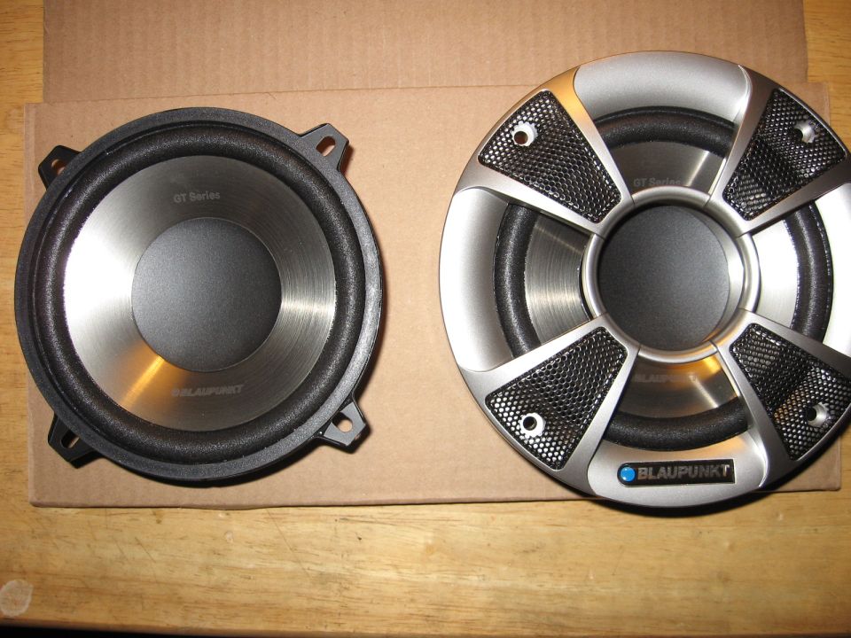 Two Blaupunkt car speakers, one with a silver grille, on a cardboard surface