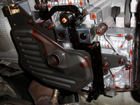 2005 Ford Crown Victoria - Close-up view of a transmission pan and filter, showing red fluid leakage.