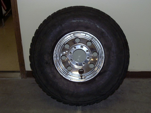 Off-road tire on polished 8-lug aluminum wheel leaning against a white wall