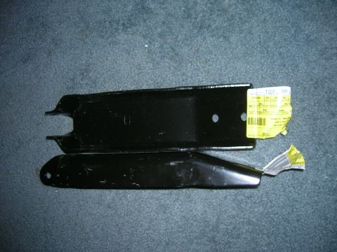 1979 Ford Bronco - Two black metal parts, possibly suspension components, lie on a textured surface with labels.