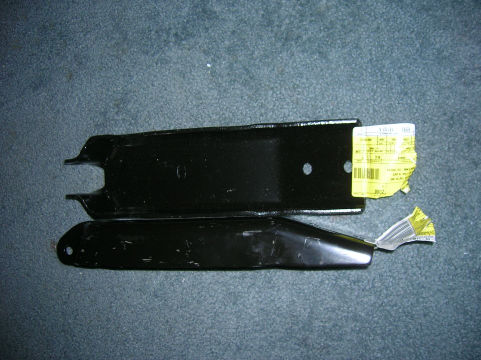 Two black metal automotive suspension components with yellow labels attached