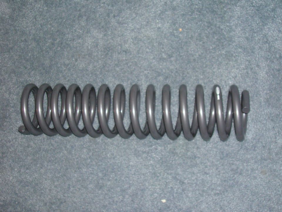 Gray coil spring on a gray carpeted surface. A small white marking is visible on one coil