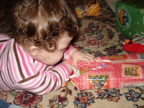 2000 Ford Crown Victoria - A baby lies on a patterned carpet, focused on opening a pink gift wrapped with cartoon characters.