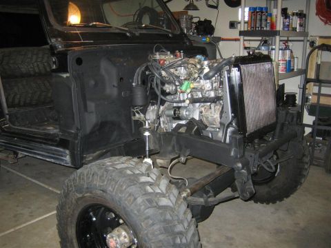 1987 Suzuki Samurai - The engine bay of a black 1987 Suzuki Samurai is shown with the engine removed, revealing the chassis and front suspension.