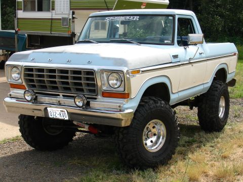 1978 Ford Bronco - This lifted 1978 Ford pickup truck features a two-tone blue and white paint scheme and a camper in the background.