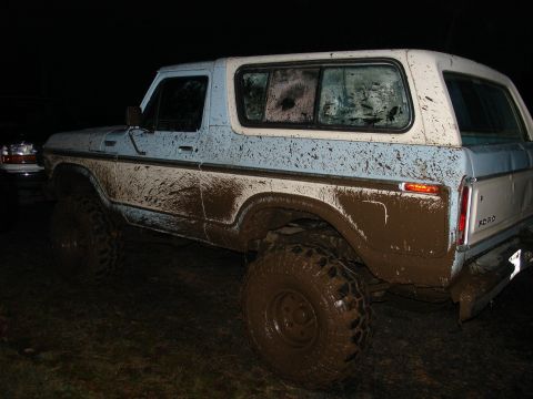 1978 Ford Bronco - A heavily mud-splattered 1978 Ford Bronco is shown off-road, with another vehicle partially visible in the background.