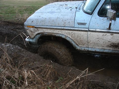 1978 Ford Bronco - This light blue and white Ford truck is stuck in deep mud, with its front tire submerged.