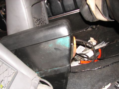 1973 Ford Ranchero - Interior view of a vehicle showing a black leather seat cushion or console pulled out, resting on dark carpet, with loose wiring, cable tie…