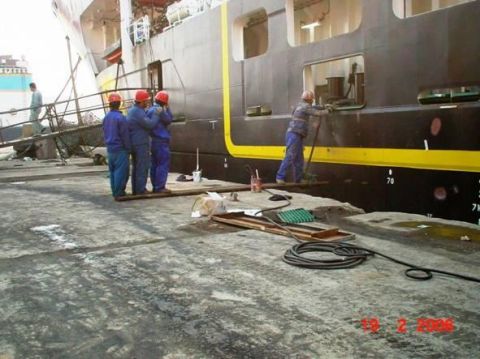 1989 Ford Bronco - Workers are performing maintenance on the side of a large ship at a dock.