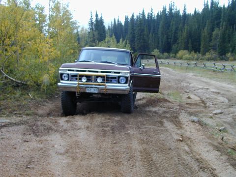 1979 Ford Bronco - This Ford F-Series truck, likely from the mid-1970s, is parked on a dirt road with trees and a wooden fence visible.