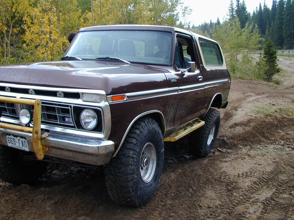 Brown Ford Bronco with yellow step bars on a dirt road