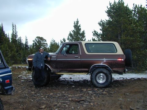 1979 Ford Bronco - A man leans against a brown 1978 Ford Bronco parked on a dirt road with trees in the background.