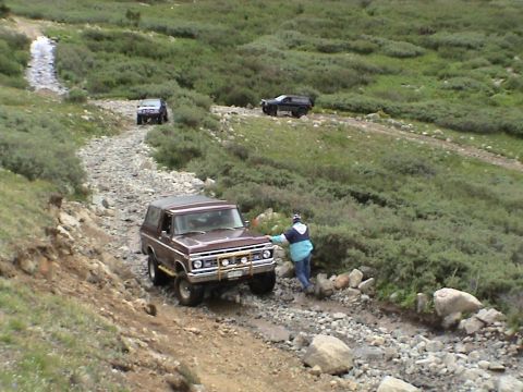 1979 Ford Bronco - A brown 1979 Ford Bronco navigates a challenging rocky mountain trail, with two other SUVs following in the distance.
