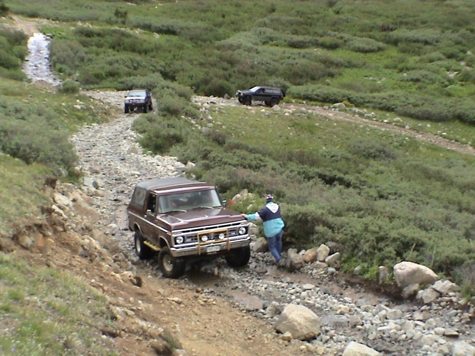 Brown 1979 Ford Bronco on rocky mountain road with two other SUVs behind