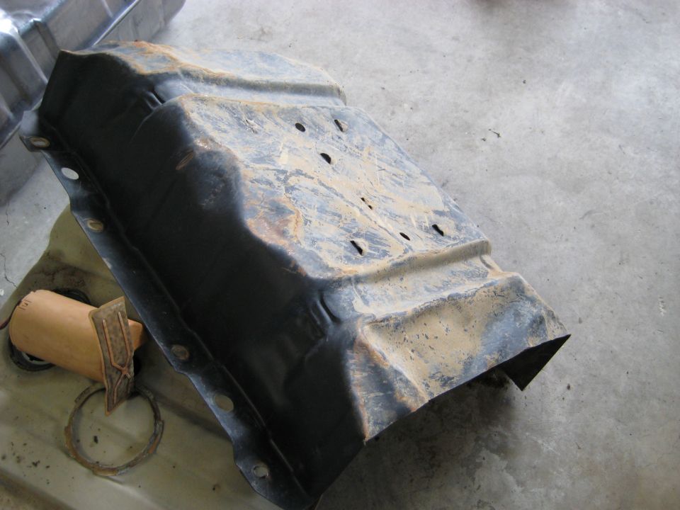 Rusty metal fuel tank with fuel pump assembly removed, lying on concrete floor