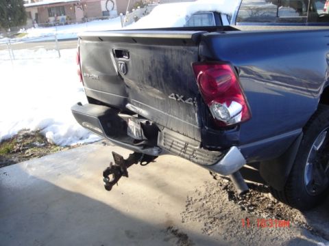 1981 Ford Bronco - The rear of a dark-colored pickup truck shows significant damage to the tailgate and bumper area.