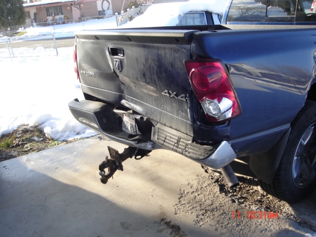Pickup truck's rear bumper and tailgate are smashed in. A trailer hitch hangs loose