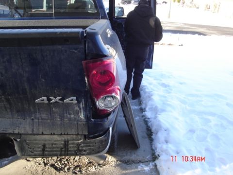 1981 Ford Bronco - A dark blue pickup truck shows damage to its rear, including a broken taillight and bumper, with a person standing nearby in a snowy enviro…