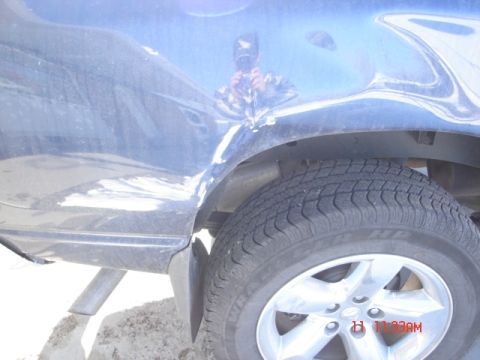 1981 Ford Bronco - The rear quarter panel of a vehicle shows significant damage, with paint chipped and metal dented near the wheel well.