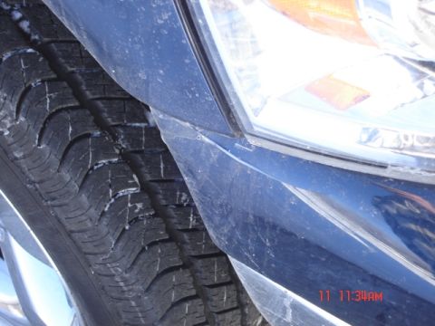 1981 Ford Bronco - A close-up view of a blue vehicle's tire and headlight assembly, showing some dirt and wear.