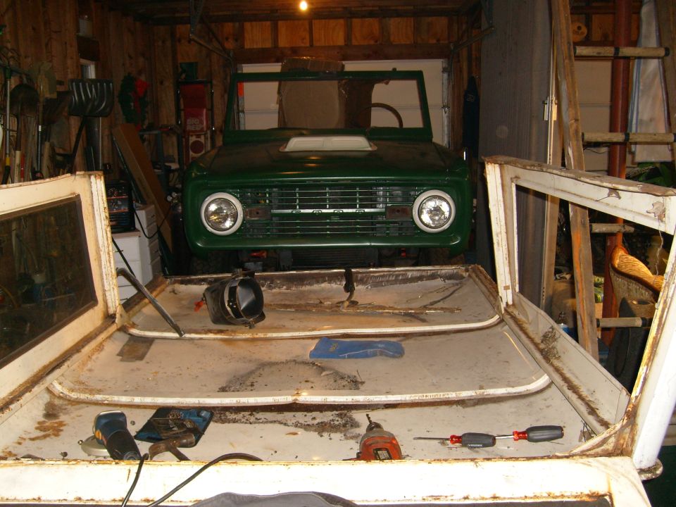 Green 1974 Ford Bronco front end in garage, disassembled with doors removed
