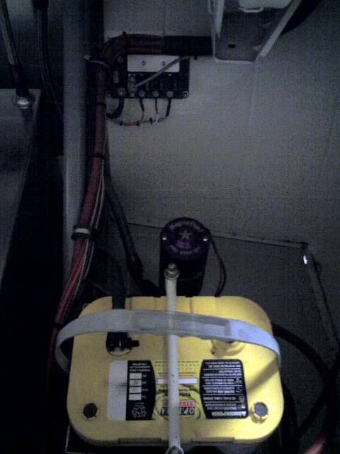 1963 Ford Fairlane - A close-up view of a yellow car battery, a black cap and associated wiring, with the SuperMotors.net logo in the lower right corner.