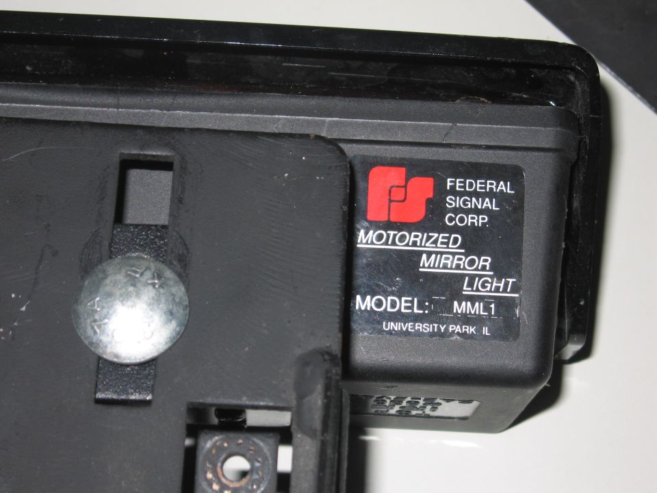 Black motorized mirror light part with a label showing Federal Signal Corp. MML1 model