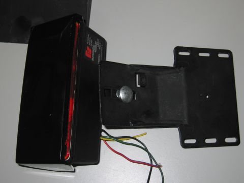 2001 Ford Crown Victoria - A close-up view of a black motorized mirror light assembly with exposed wiring and a red reflector strip.