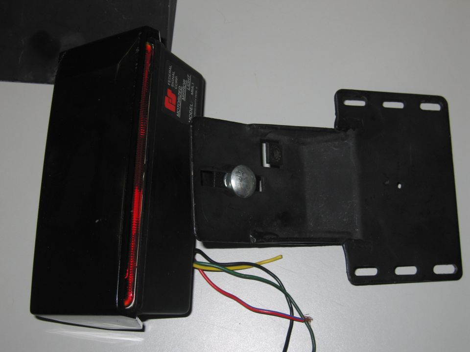 Black motorized mirror light with red reflector and wires. Text on side reads FEDERAL SIGNAL MOTORIZED MIRROR LIGHT MODEL MRL1