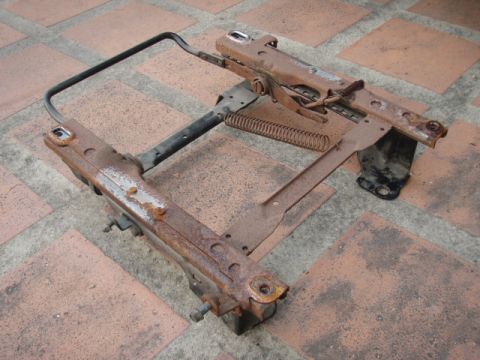1995 Ford F-150 - A corroded vehicle seat frame lies on a tiled surface, showing signs of wear and tear.