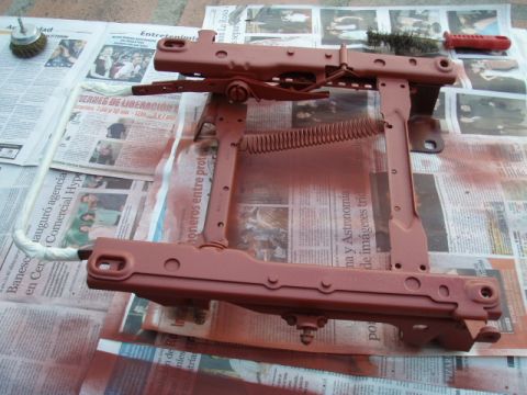 1995 Ford F-150 - A vehicle seat frame is being painted red, laid out on newspapers with tools.